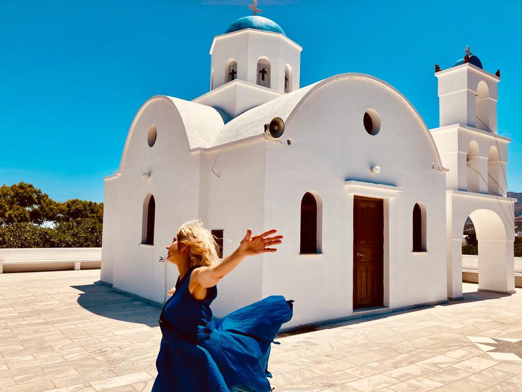 Hayley Enright with arms open in front of a whitewashed church
